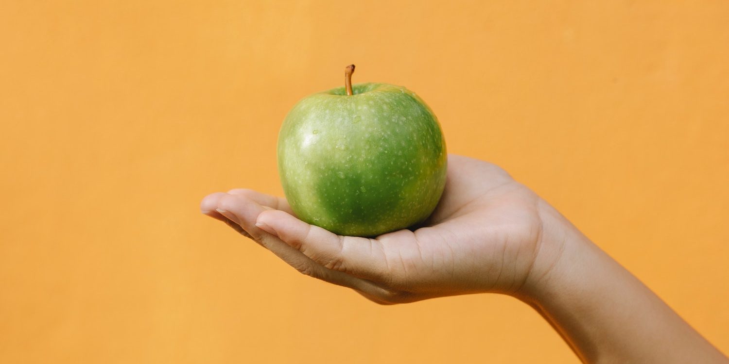 Green apple held by woman's hand representing the Nourish Phoenix food and clothing bank branding.